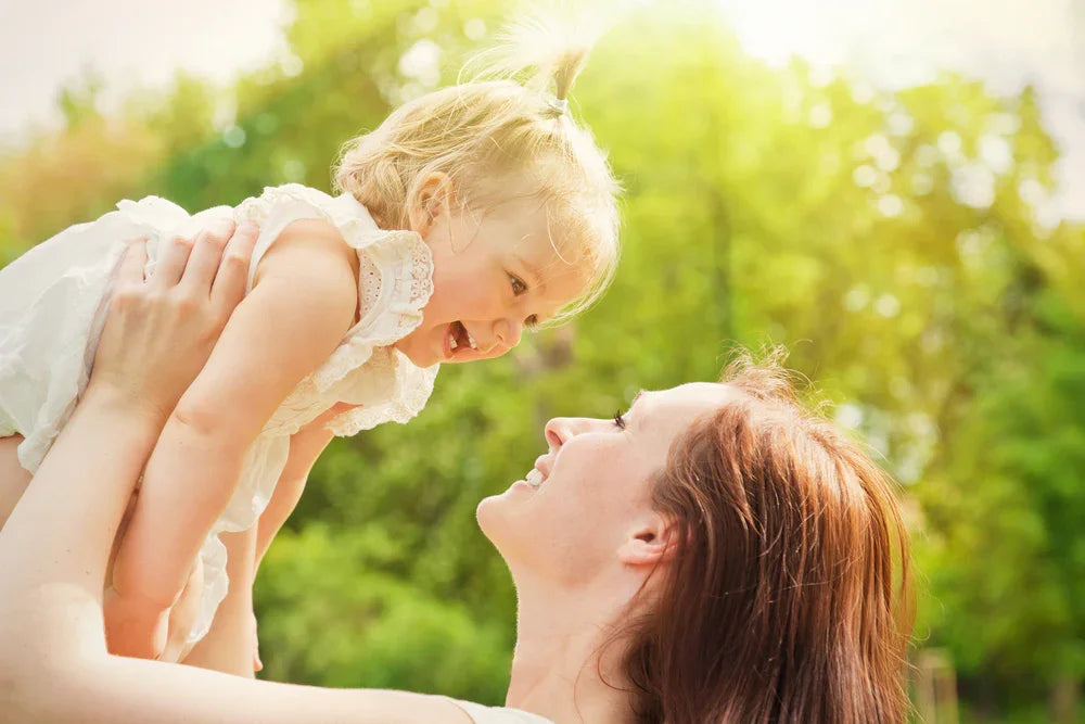 Woman holding a child outdoors with greenery in the background